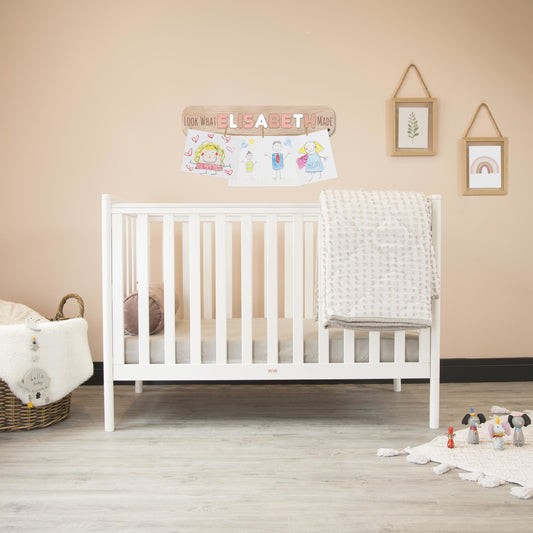 White crib in a nursery with decor elements on the wall.